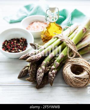 Bunch of raw asparagus stems with different spices and ingredients on wooden background. Top view, flat lay. Stock Photo