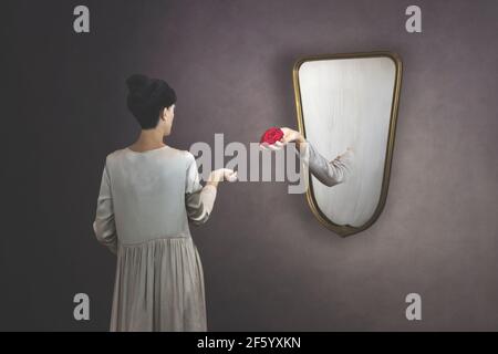 surreal gesture of a hand coming out of the mirror to give a rose to a woman Stock Photo