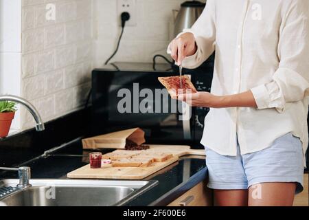 Cropped image of young woman making sweet sandwich and spreading berry jam on bread Stock Photo