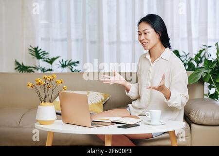 Pretty positive young Asian woman having online meeting with coworkers or fellow students Stock Photo