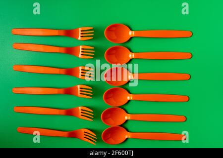 Plastic orange spoons and forks on green background. Eco friendly and plastic free concept. Stock Photo