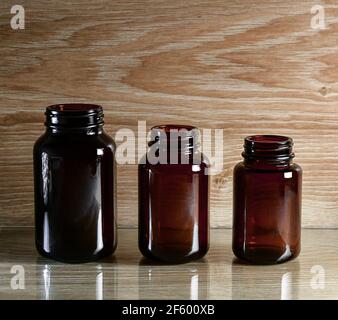 Three glass cans of dark glass bottles. Empty, lined in a row in height, on a wooden surface with glitter and reflection. Stock Photo