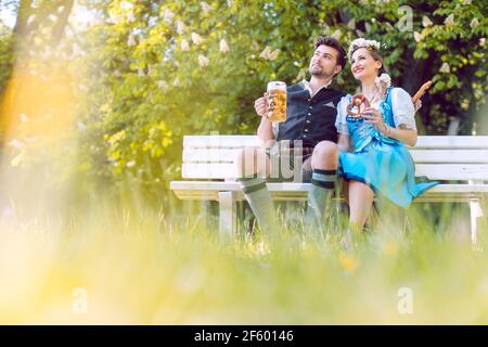 Couple in Bavaria sitting on bench toasting with beer Stock Photo