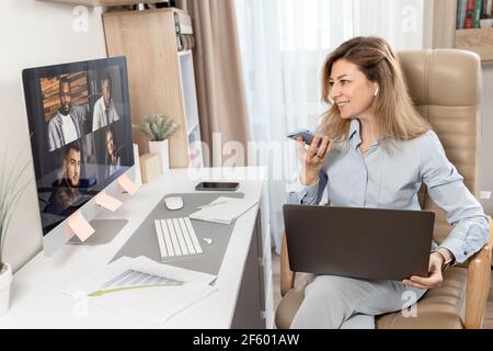 Happy business lady is working from home office, having a video meeting, smiling. Beautiful successful female is sitting at the desk, recording voice Stock Photo
