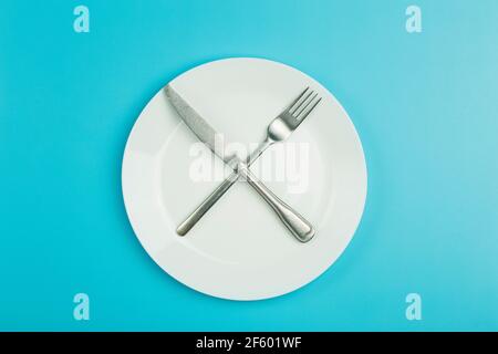 Empty plate on a blue minimal background. Empty white ceramic plate with knife and fork on the table after eating. Diet and healthy food concept. High quality photo Stock Photo