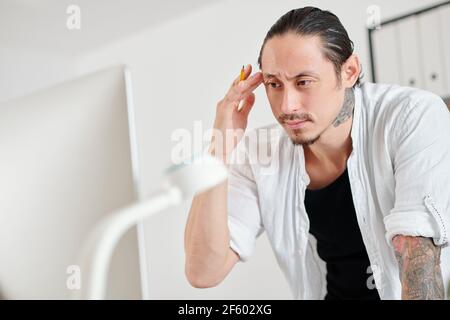 Frowning serious graphic designer reading e-mail from client on computer screen Stock Photo