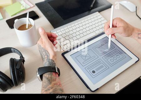 Hands of UI designer working on interface of new website or mobile application, he is pointing at tablet computer with digital pen Stock Photo