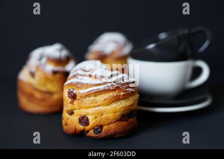 Fresh Easter bakery or tea time concept. Cute tasty cruffins with raisins and white sugar powder on it with black and white coffee cups near them. Black background. High quality photo Stock Photo
