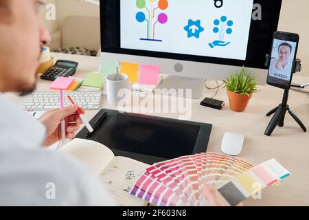 Graphic designer having video call with client when working on logotype for his company and choosing color from palette Stock Photo