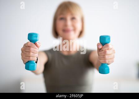 Senior woman doing fitness exercises with weights at home, focus on hands holding dumbbells Stock Photo