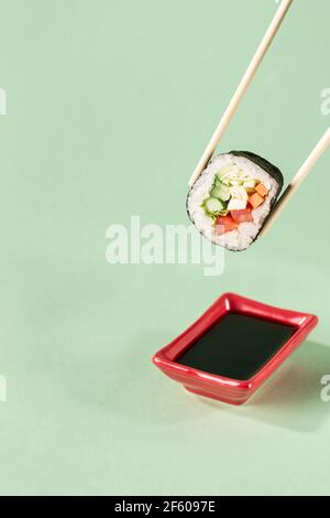 Rolls with fresh vegetables with chopsticks with a plate for soy sauce on a bright green background, side view with a copy space for text. Vegan sushi