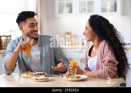 Cheerful Arab Couple Chatting And Laughing While Having Breakfast In Kitchen Stock Photo