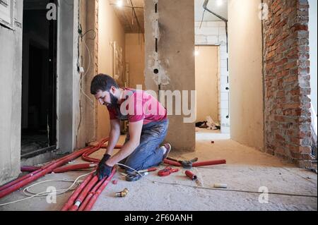 Young bearded plumber installing underfloor heating system in new apartment Stock Photo