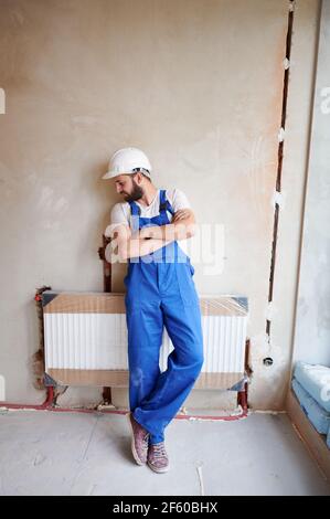 Young handsome plumber installing water radiator in unfinished apartment Stock Photo