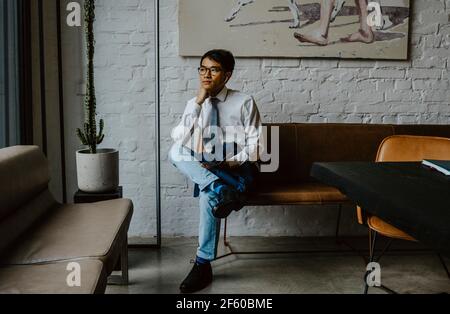 Businessman sitting over sofa with hand on chin at office Stock Photo