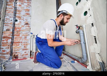 Young plumber working with grey sewer pipes, fixing them to wall Stock Photo