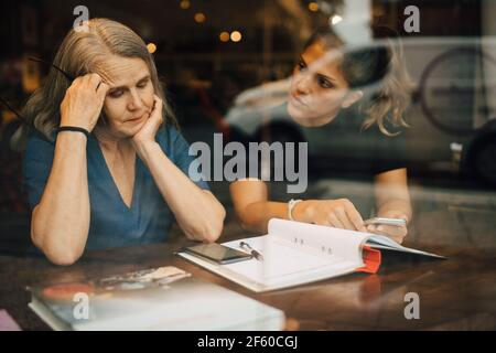 Female coworkers discussing seen through glass of retail store Stock Photo