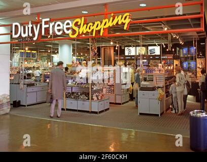 Historical 1987 archival view of illuminated store sign above Duty Free shopping premises shows interior shop design of an 80s Departure lounge inside building with travelling shoppers browsing brands of merchandise before flying out form Gatwick Airport West Sussex England UK an archive image of the way we were in the 1980s Stock Photo