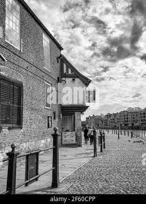 Riverside pub in York.  The ancient building is beside a cobblestone path and some people walk past. Cloudy sky is above. Stock Photo