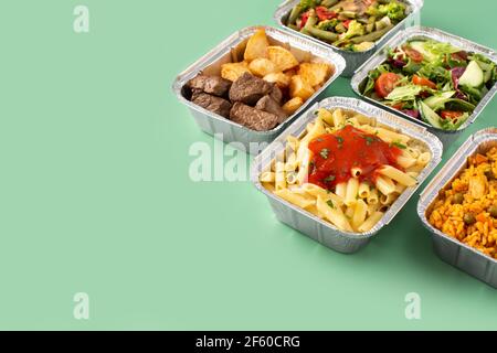 Take away healthy food in foil boxes on green background Stock Photo