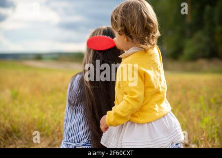 adorable toddler girl combing her mom's hair outdoors outdoors on a sunny day. mother and daughter love concept Stock Photo