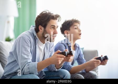 Leisure with dad. Concentrated father and son competing with each other in online video games, using joysticks Stock Photo