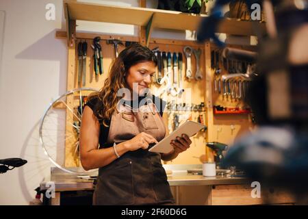 Smiling female owner using digital tablet at bicycle workshop Stock Photo