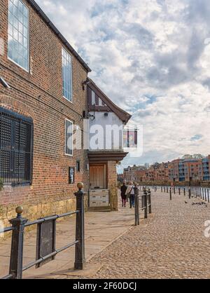 Riverside pub in York.  The ancient building is beside a cobblestone path and some people walk past. Cloudy sky is above. Stock Photo