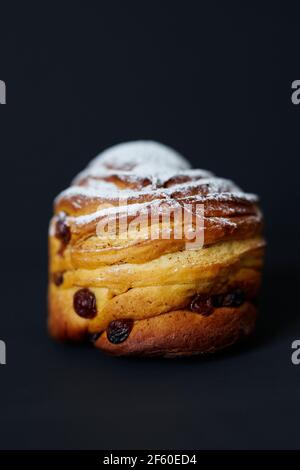 Cute cruffin with raisins and white sugar powder on it on black background. Fresh Easter pie or bakery concept. High quality photo Stock Photo