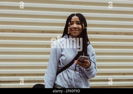 Portrait of smiling teenage girl with smart phone against wall Stock Photo