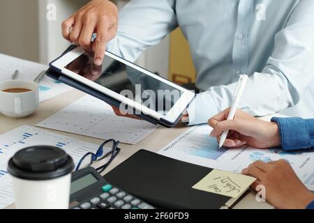 Close-up image of businessman pointing at screen of tablet computer when showing product presentation he created to colleague Stock Photo