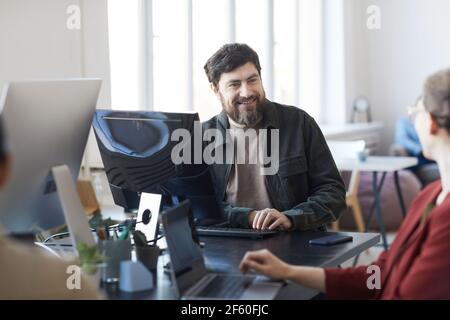 Portrait of smiling bearded man talking to colleagues during meeting in modern IT office, copy space Stock Photo