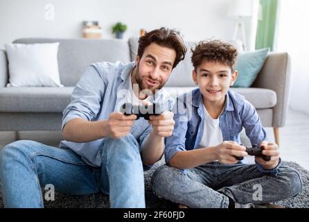Cozy family weekend. Overjoyed father and son competing in online video games, spending time together at home Stock Photo