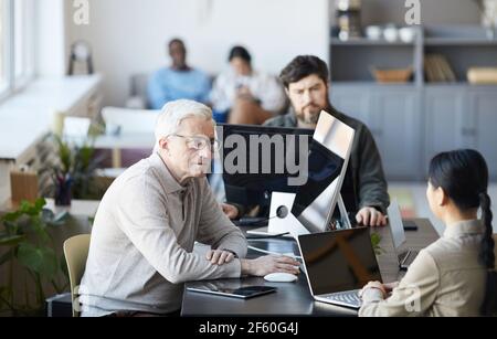 Portrait of white haired senior man collaborating with young people in modern office, career change concept, copy space Stock Photo