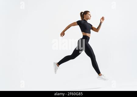 Woman runner in silhouette on white background. Dynamic movement. Side view of female jogger, sportswoman in sport clothing in air, jumping or running Stock Photo