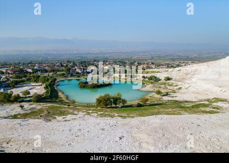 Panoramic view onto lake near foot of famous travertines of Pamukkale (Turkey) & town itself. Green & blue color of water formed by mineral water