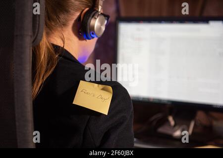 Pasting aprils fools day sticker on woman shoulder while busy on PC work - concept of April fool day celebration Stock Photo