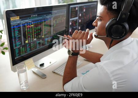 Serious trader in headset checking financial graphs on computer screens, investment concept Stock Photo