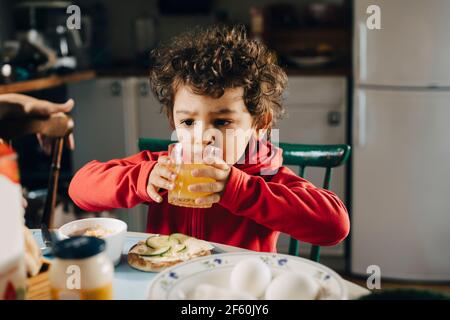 Cute boy drinking juice while sitting by table during breakfast Stock Photo