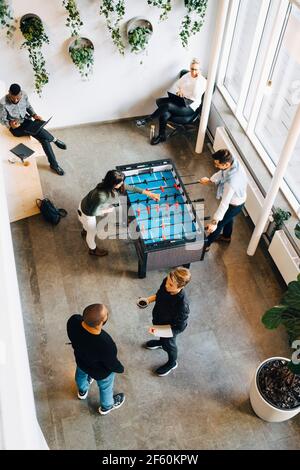 Male and female colleagues playing foosball while taking break from work in office Stock Photo