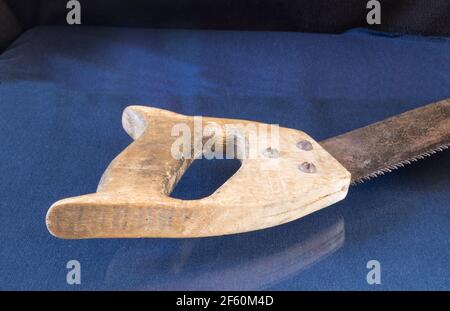 A saw with a wooden handle lies on a table with a reflection. Carpenter's tool on a blue background Stock Photo