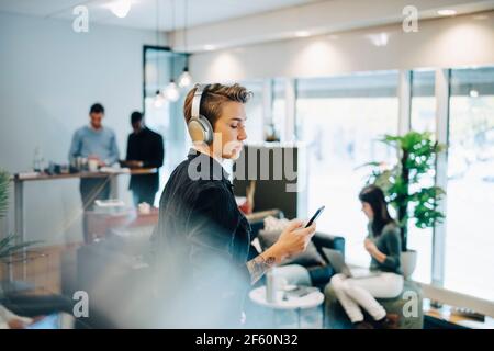 Female entrepreneur using smart phone while colleagues working in background Stock Photo