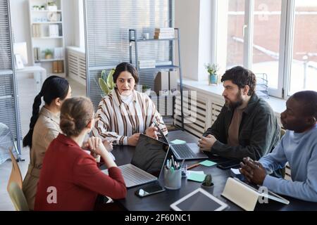 Portrait of diverse group of business people at table collaborating during briefing meeting in office, focus on Middle-Eastern female manager Stock Photo