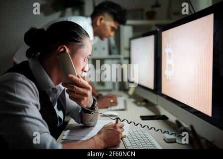 Serious trader talking on phone with client when looking at bitcoin price chart watch for trading opportunities Stock Photo
