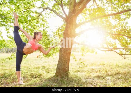 Young woman doing leg stretching before yoga exercises in nature on a tree in summer Stock Photo