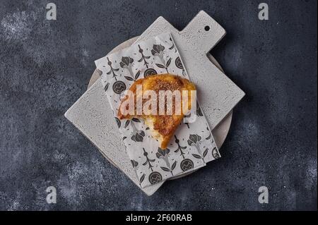 Broken piece of torrijas on craft paper on ceramic cutting board on dark background. Top view. Copy space Stock Photo