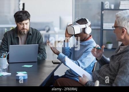 Side view portrait of African-American man wearing VR headset during meeting with diverse IT team in office Stock Photo