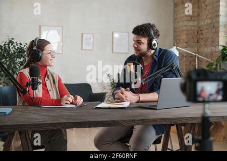 Young man in headphones interviewing a woman at the table during broadcasting at radio studio Stock Photo