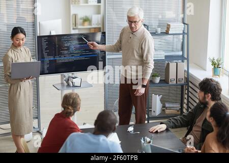 Portrait of modern senior man giving presentation in office to diverse IT team and pointing at code on screen, copy space Stock Photo