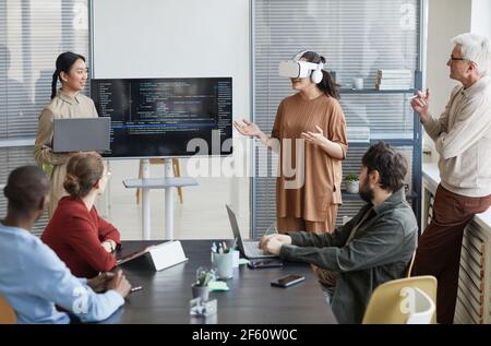 Portrait of diverse IT development team working on virtual reality software, focus on smiling woman wearing VR headset in office Stock Photo